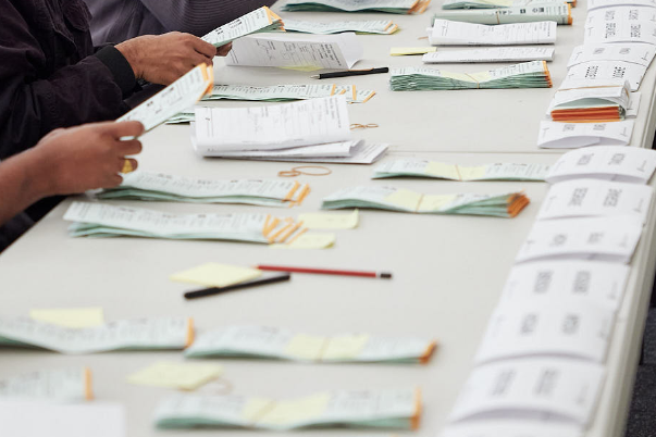 Ballot papers spread out on a table sorted into piles.