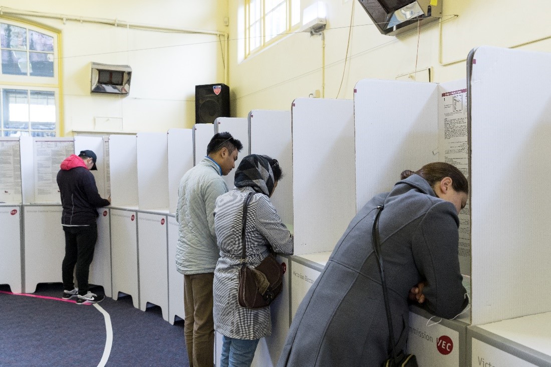 Four people voting at private voting screens inside a voting centre.
