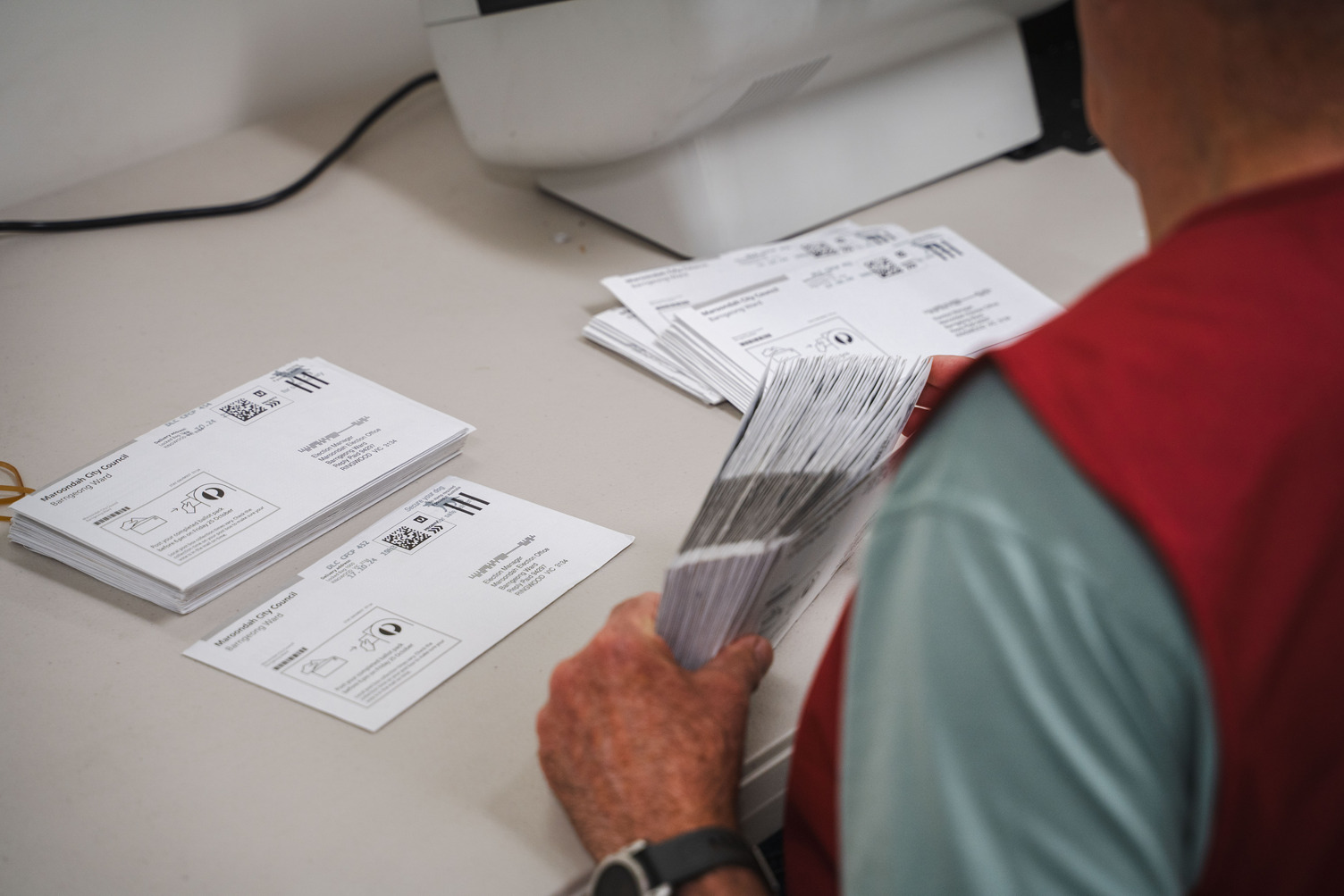An election officer wearing a red vest sorts through postal vote envelopes for Maroondah City Council.