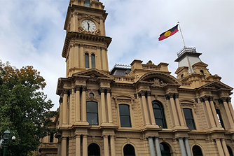 Frontage of a heritage town hall with columns, a clocktower and the Aboriginal flag