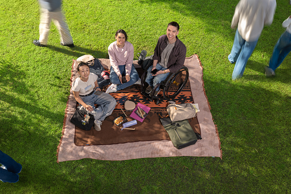 Three students on a picnic rug on the grass