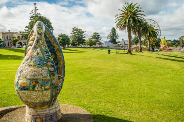 Glenelg Shire Council, Portland foreshore. Green grass and palm trees with a mosaic sculpture in the foreground.