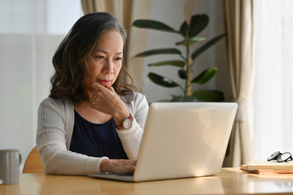 Person seated at a table using a laptop, with a notebook and glasses on the table beside them.