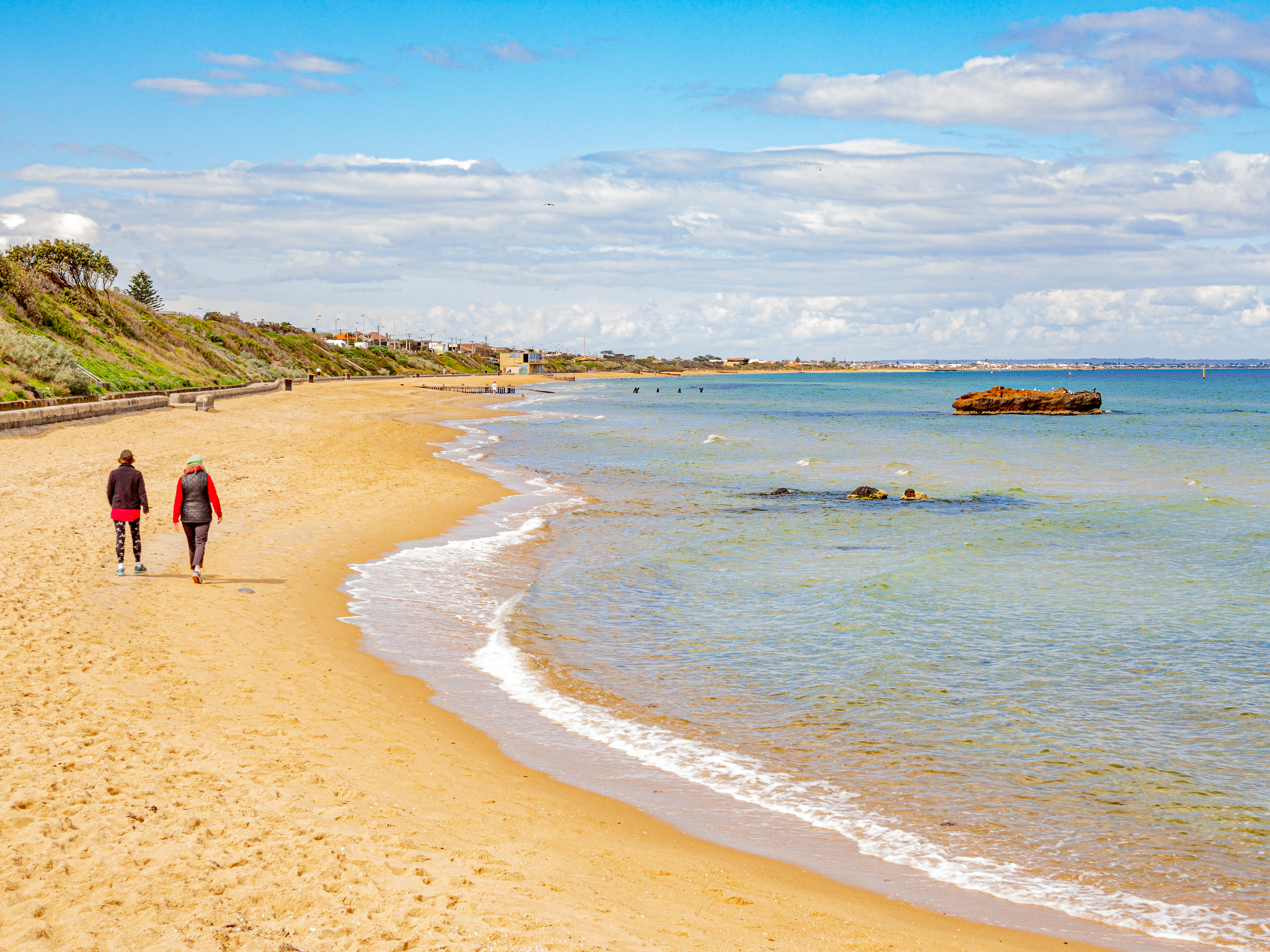 Two people walking on a beach with clear blue water