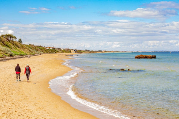 Two people walking on a beach with clear blue water